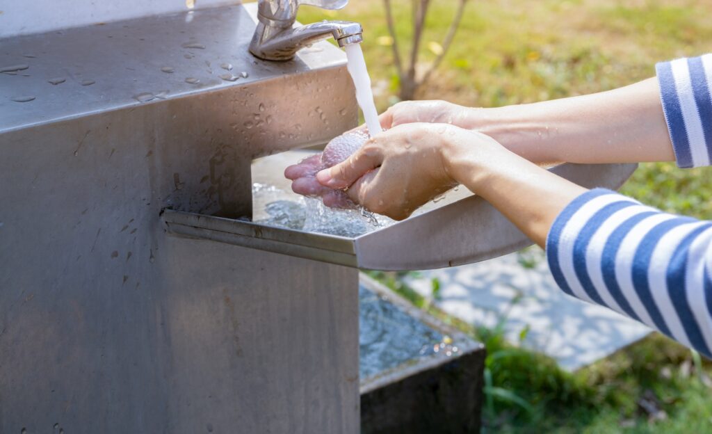 Woman washing hands with tap water under faucet at stainless steel sink.