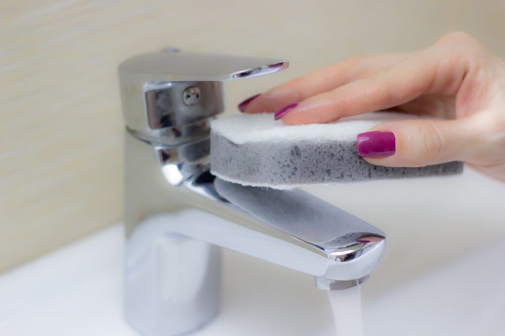 Woman cleaning tap with sponge